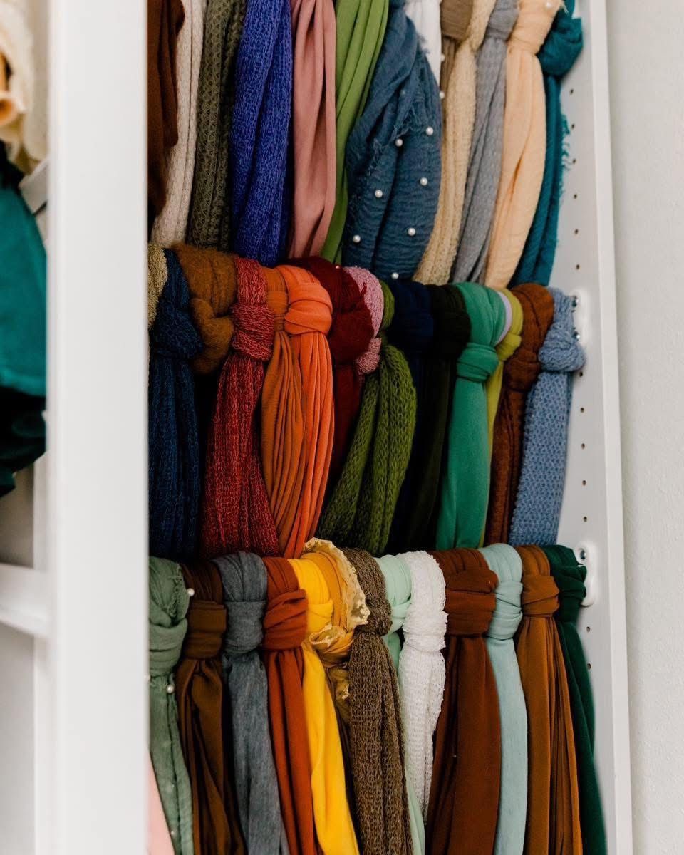 Colorful scarves and wraps neatly organized on shelves in a closet, arranged by color.