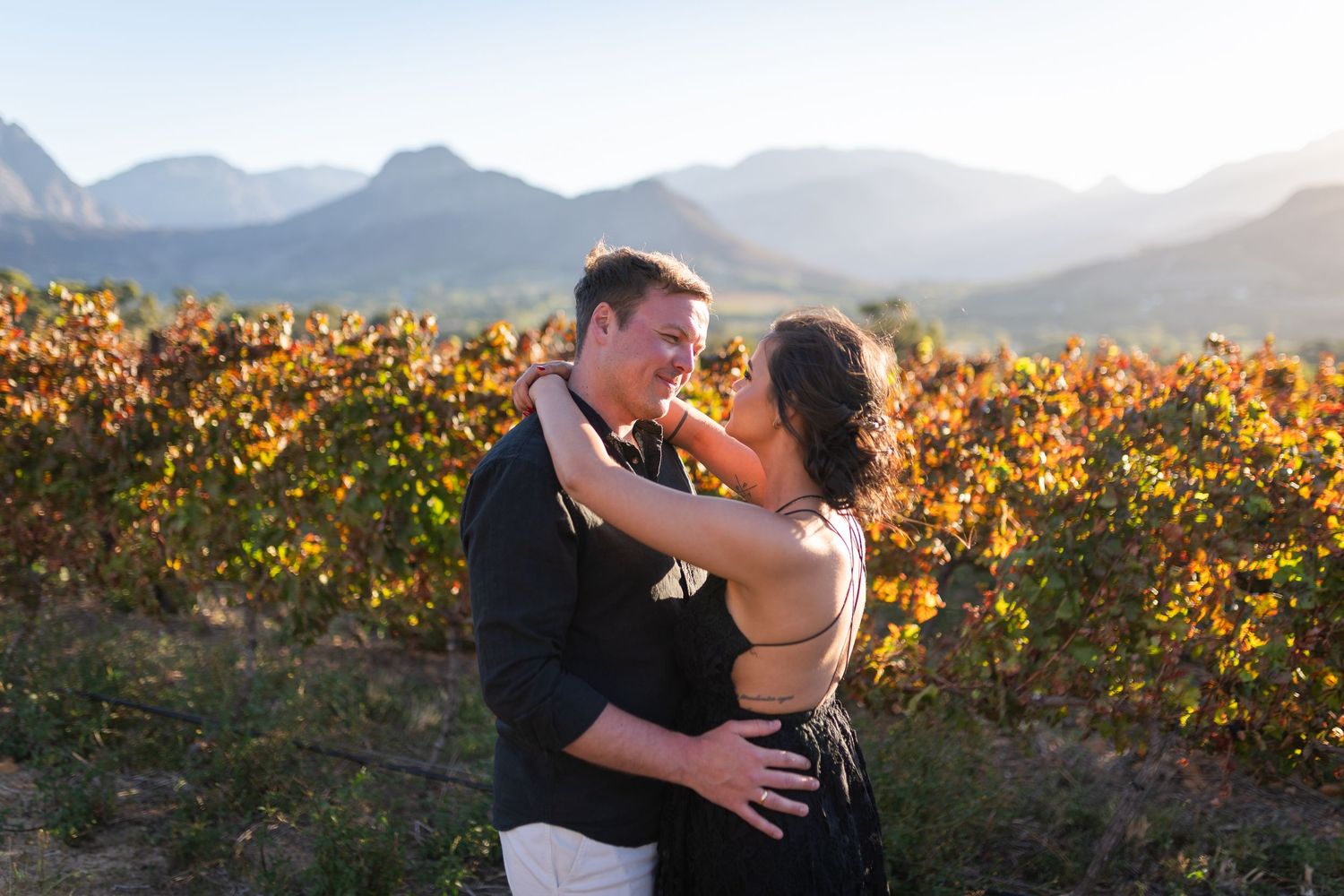 Couple sharing a romantic kiss among lush vineyard rows on their wedding day in a sunny outdoor setting.