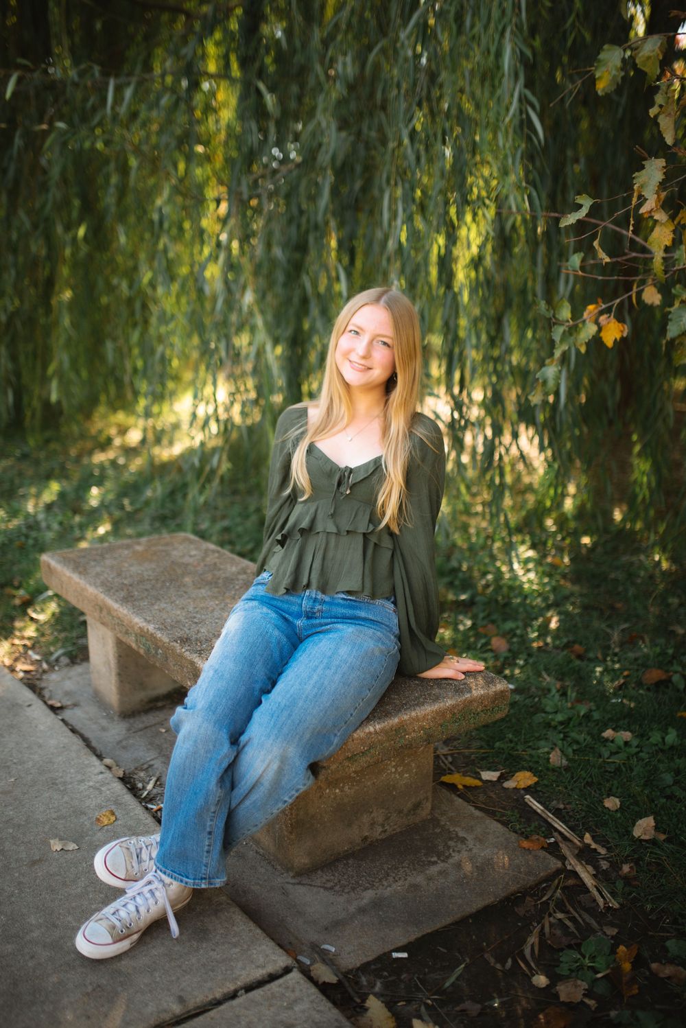 Person sitting on stone steps surrounded by drooping willow tree branches in an outdoor garden setting.