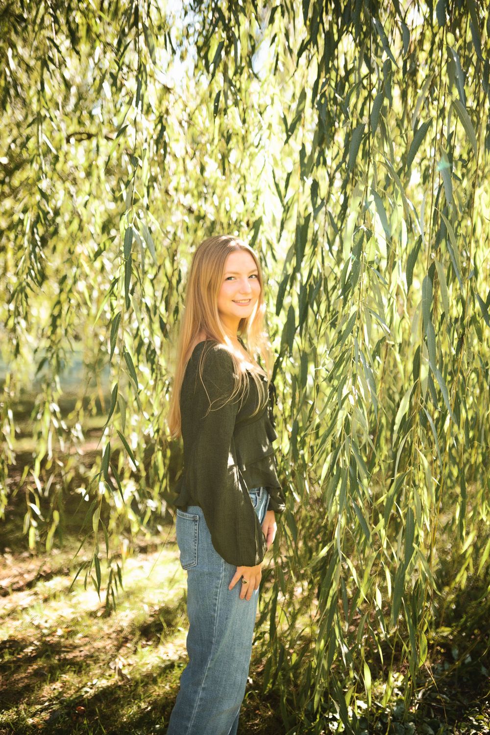 A casual outdoor photoshoot under drooping willow tree branches with soft natural lighting.