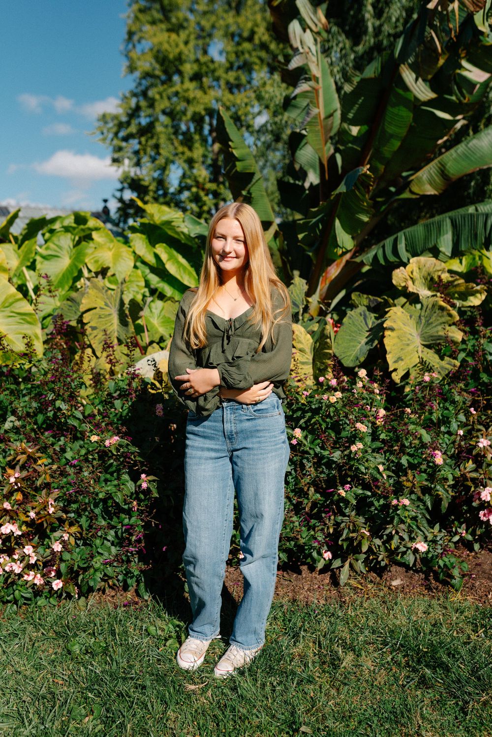 A casual outdoor photoshoot in a garden setting with lush greenery and blooming flowers in the background.