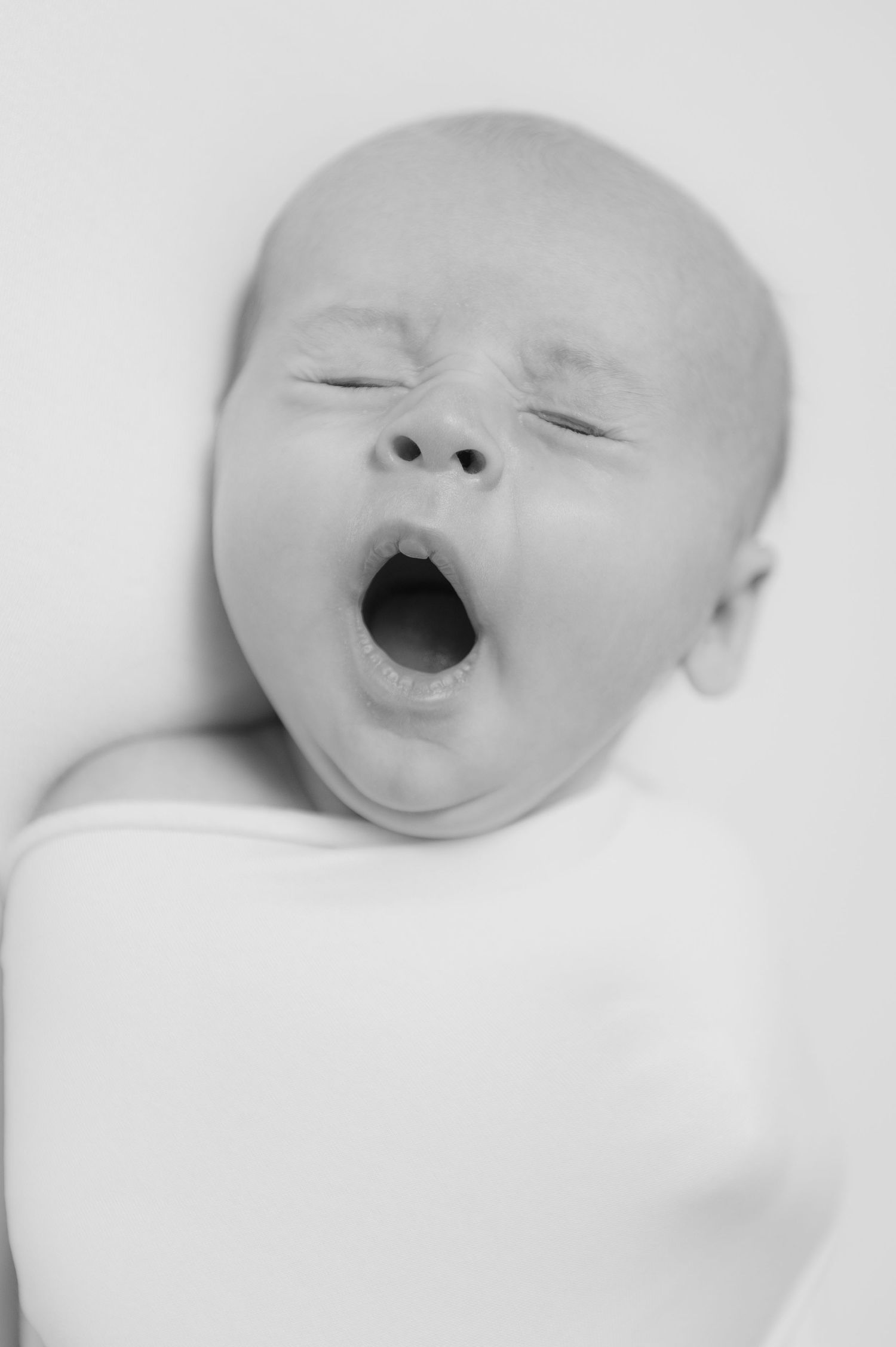 Black and white close-up of a yawning baby with closed eyes against a white background.