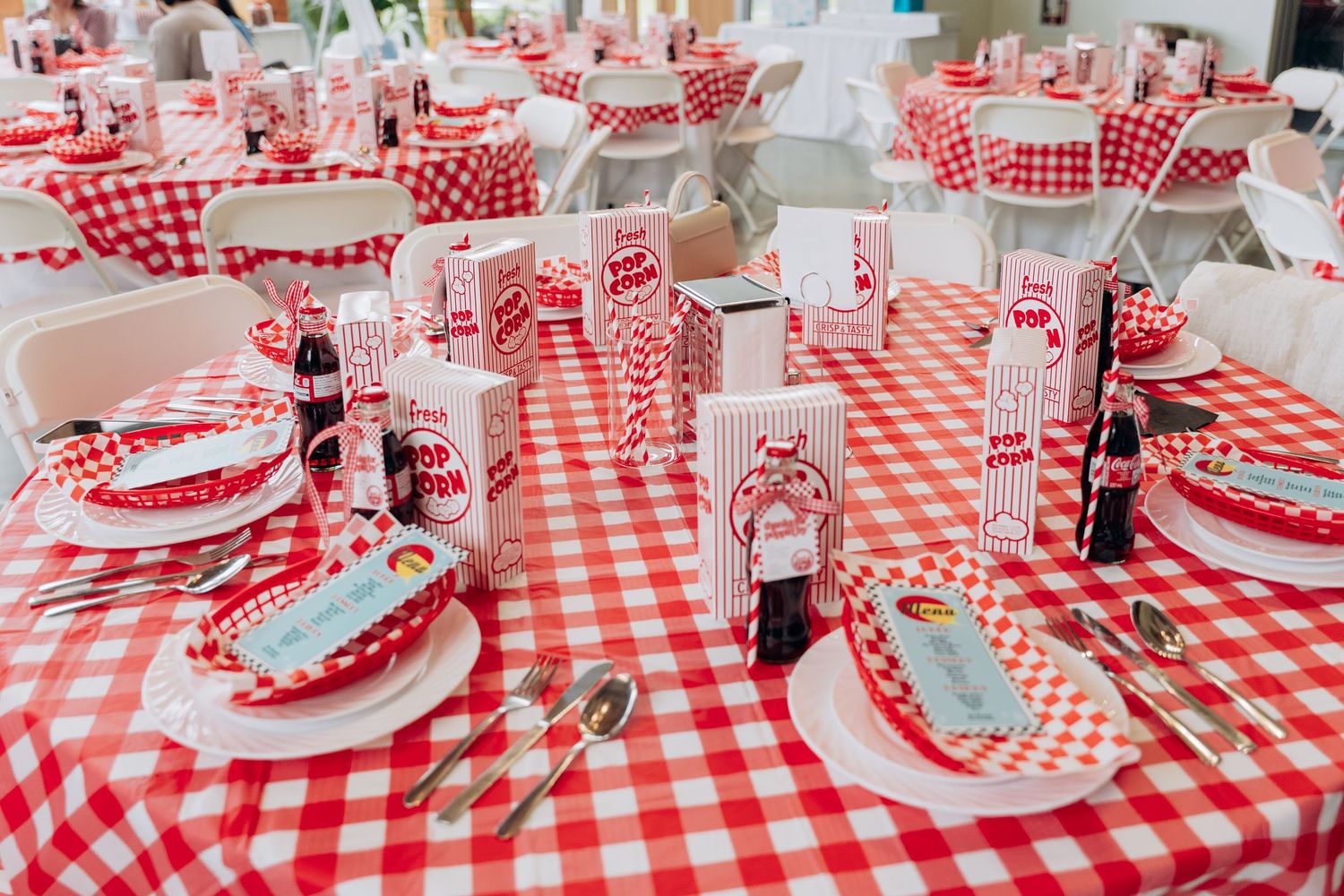 Long tables set with red and white checkered tablecloths and place settings for a casual dining event.