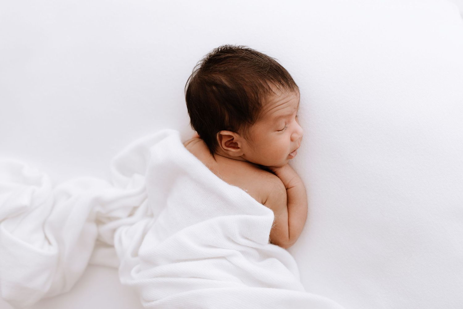 Minimalist newborn photography on white bedding showing peaceful sleeping baby.
