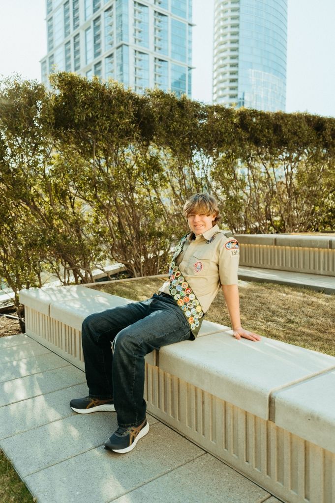 A scout resting on a concrete wall in an urban setting with high-rise buildings in the background.