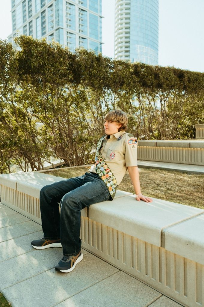 Person in casual attire relaxing on a concrete ledge in an urban setting with tall buildings in the background.