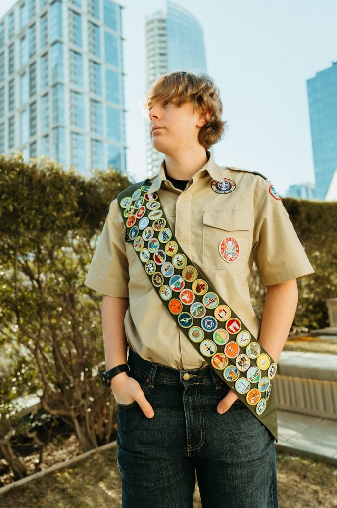 Close-up view of a tan scout uniform showing colorful merit badges and patches on the sash.