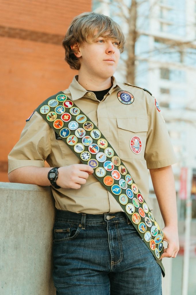 A Boy Scout wearing a khaki uniform and sash displays an impressive collection of merit badges earned through scouting achievements.