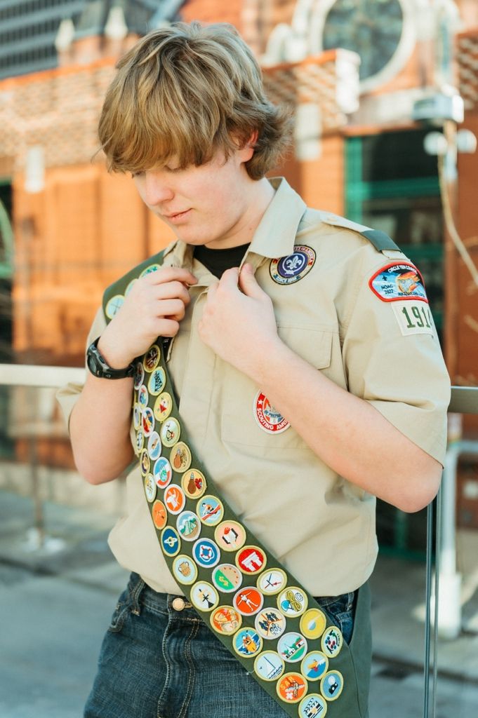 Close-up view of Boy Scout merit badge sash with colorful patches against tan uniform.