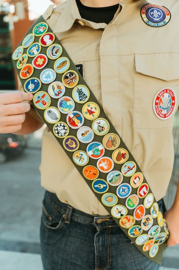 A Boy Scout merit badge sash displaying numerous colorful circular achievement patches on a tan uniform.