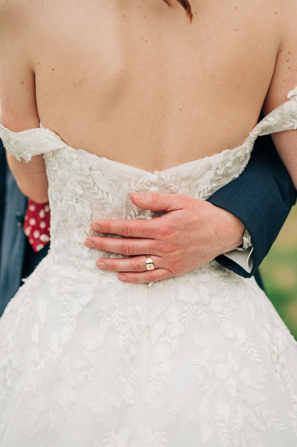 Close-up of wedding dress back detail showing lace pattern and hands with new ring.