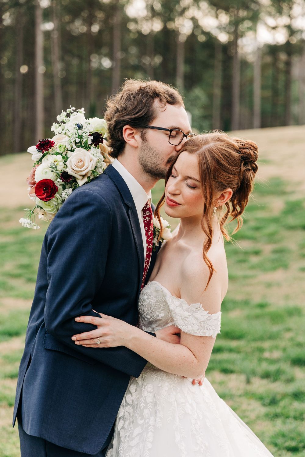 Romantic wedding couple embracing in outdoor portrait session with natural lighting and floral bouquet.
