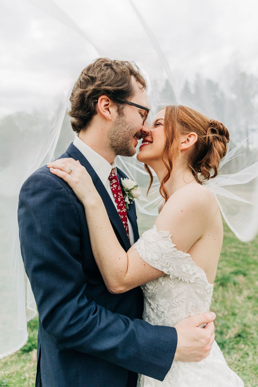 Romantic wedding portrait with flowing veil against soft cloudy sky.