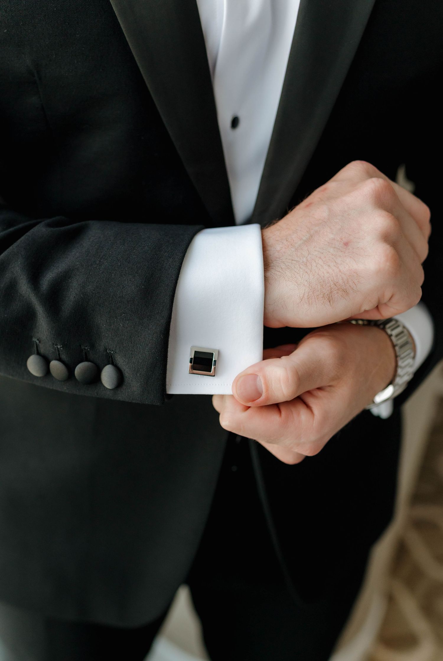 Close-up view of hands adjusting a black cufflink on white dress shirt sleeve with formal tuxedo jacket.
