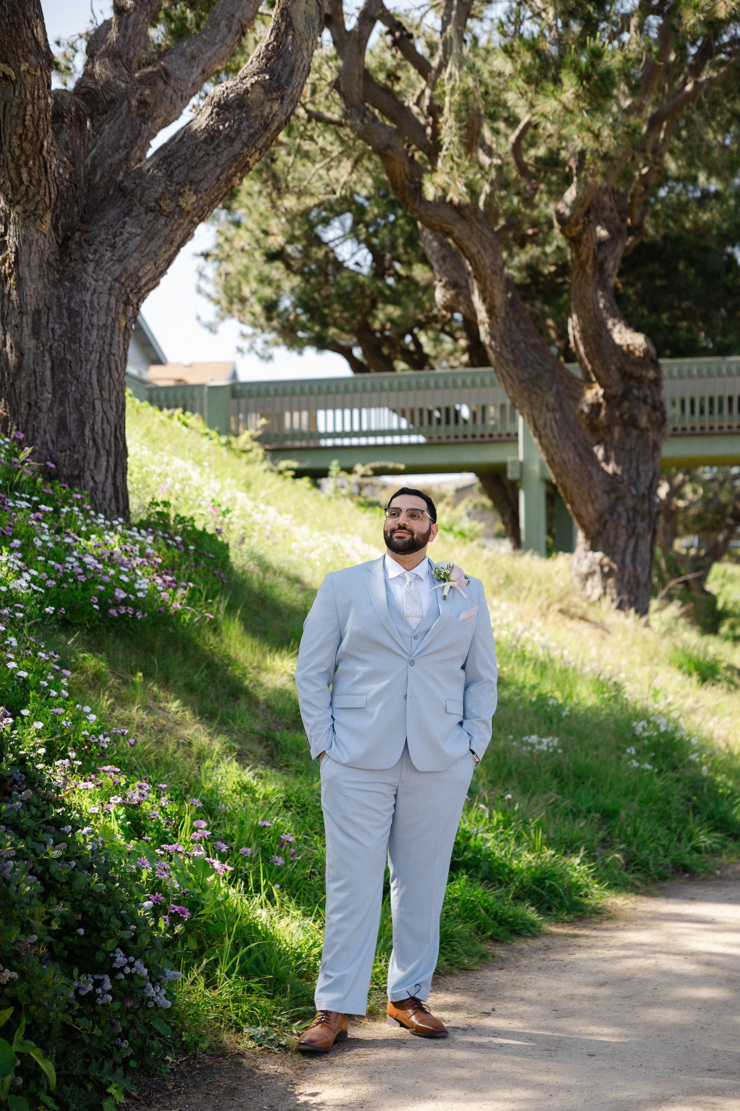 A person in a navy suit poses among towering redwood trees in a forest setting.