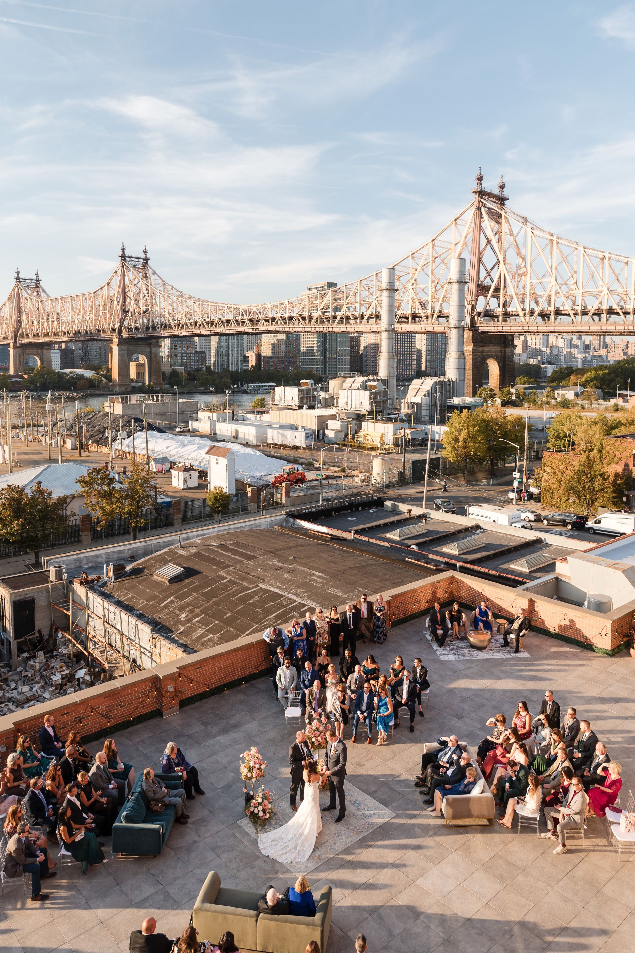 Rooftop wedding ceremony with guests seated outdoors, featuring the Queensboro Bridge and NYC skyline backdrop.