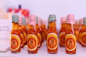 Small bottles of orange hot sauce with decorative labels displayed in rows on a white surface.