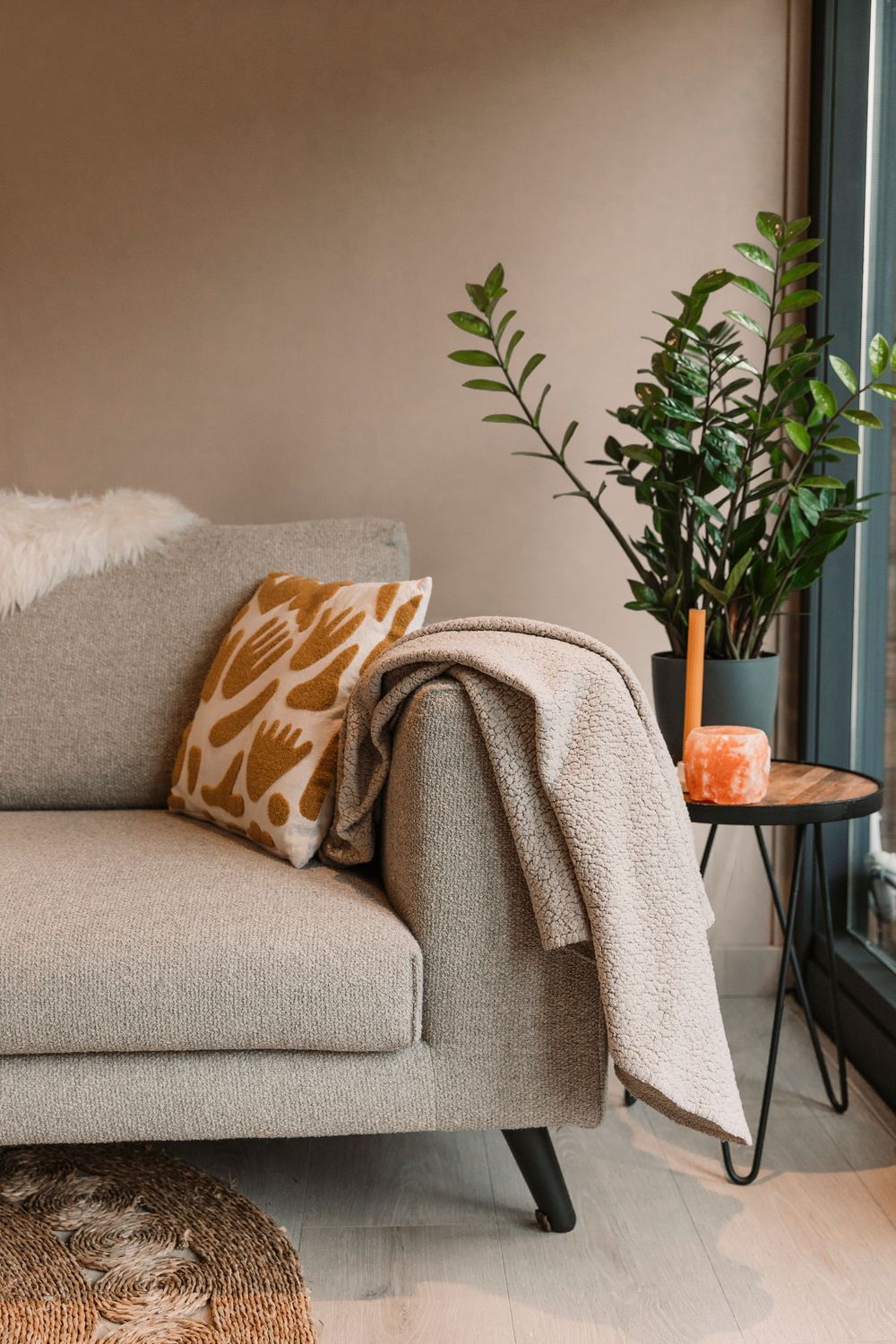 Cozy gray couch with orange accent pillow and throw blanket next to potted plant by window.
