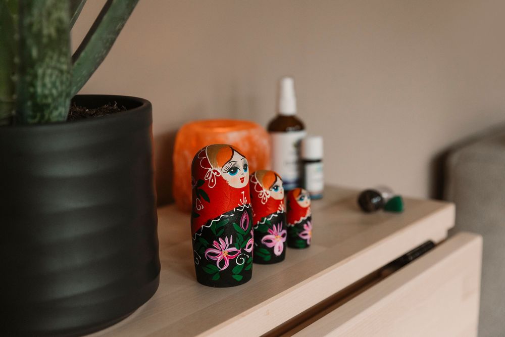 Decorative red nesting dolls displayed with plants and bottles on shelf.