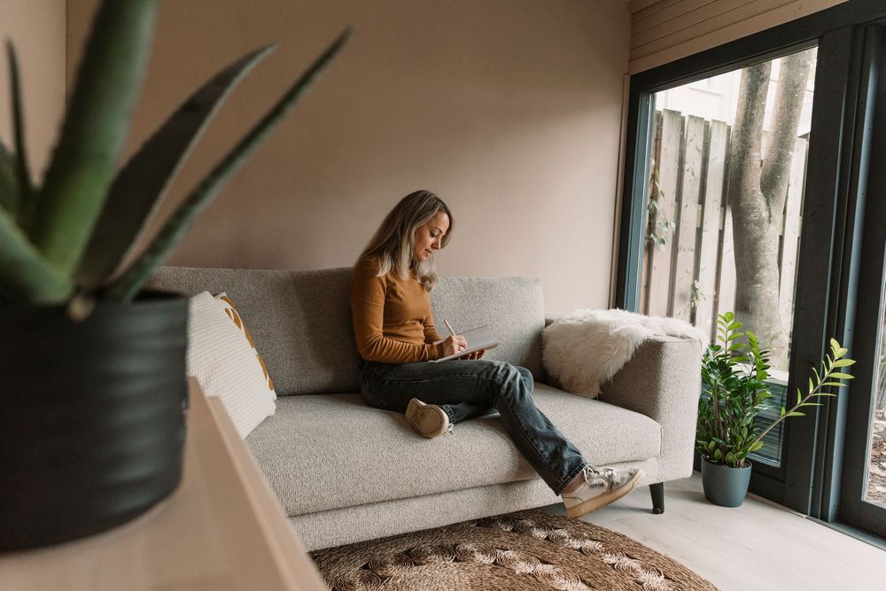 Cozy living room corner with gray couch, plants and natural light.