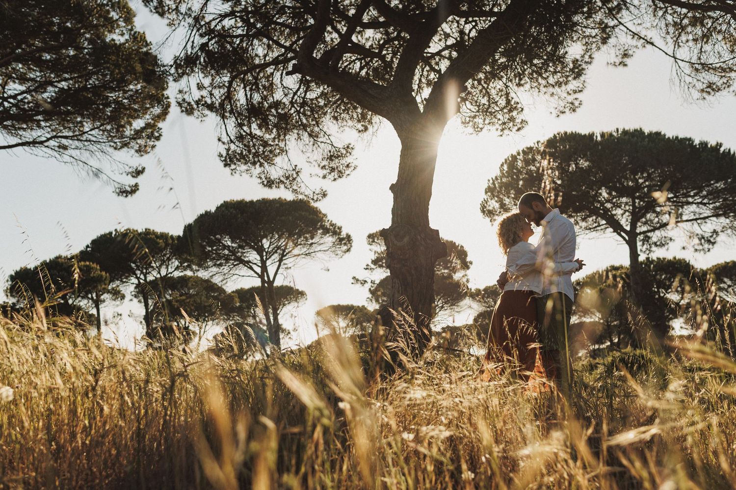 Couple kissing in golden hour light surrounded by wild grass in Portugal coastal landscape