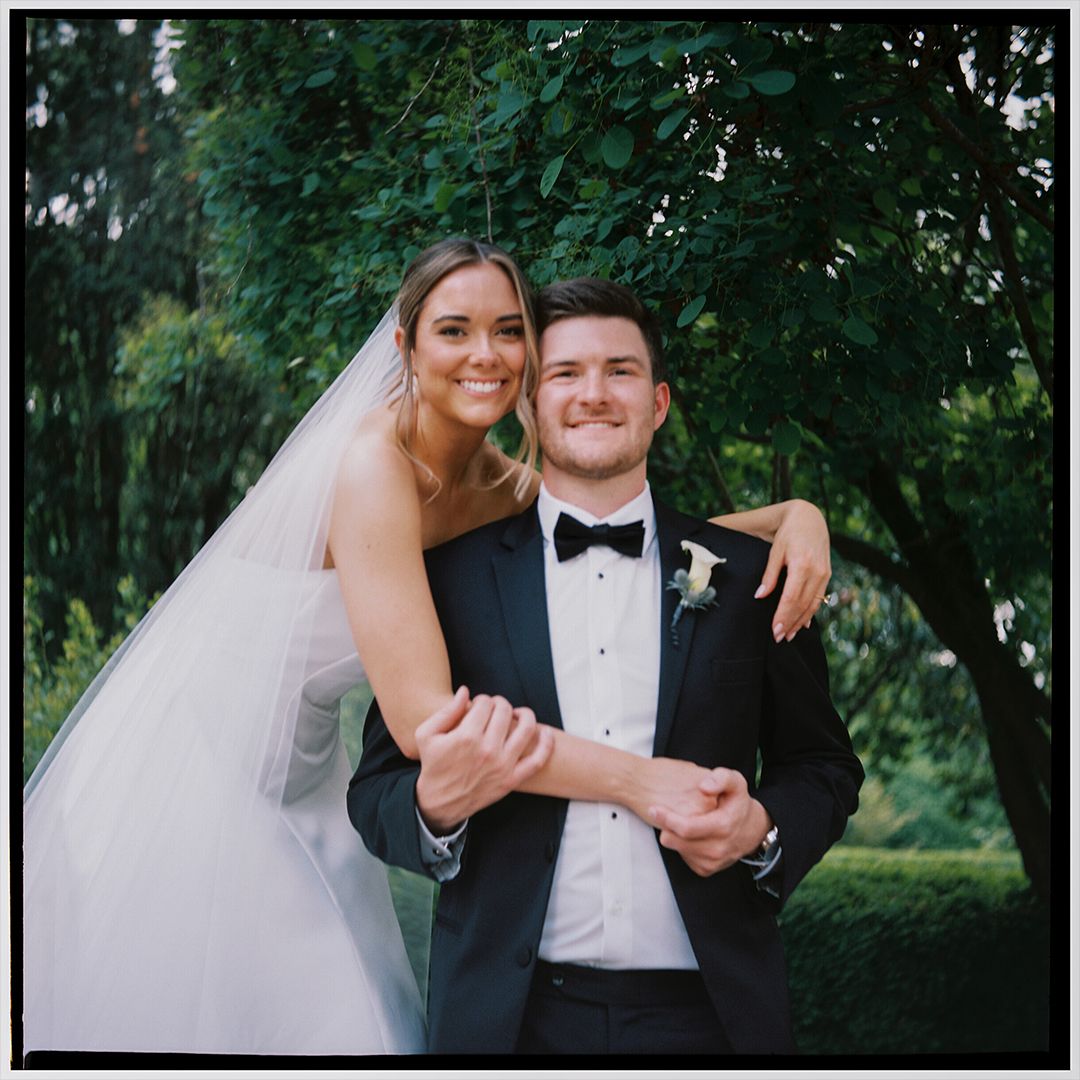 Couple in wedding attire sharing intimate moments outdoors in a garden setting with natural greenery backdrop.