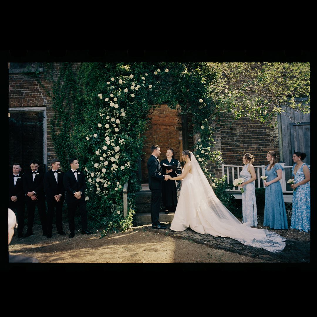 Wedding party poses together in garden setting with blooming white flowers and greenery creating a romantic backdrop.