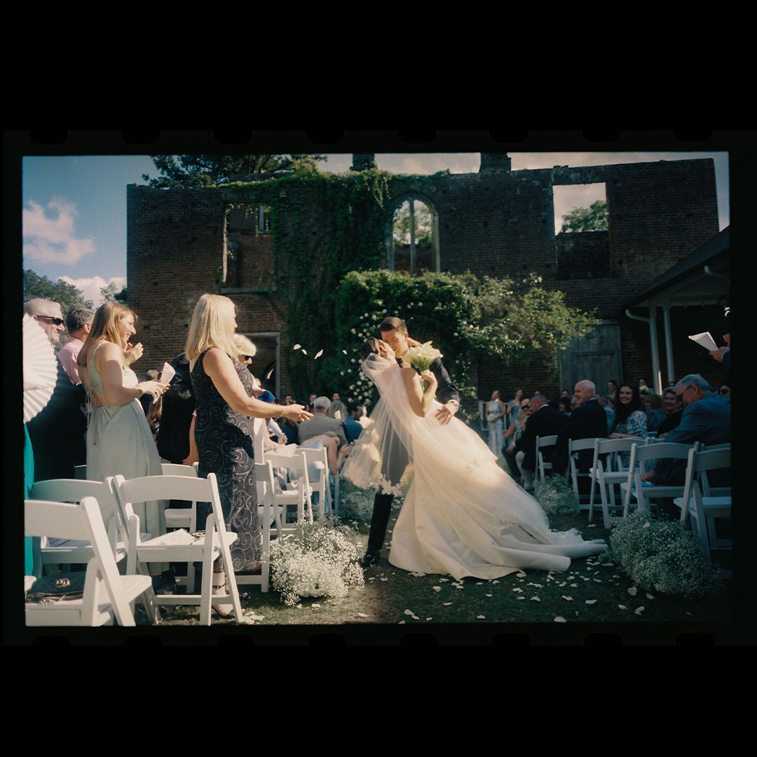 Wedding guests seated outdoors at a garden ceremony with white chairs arranged in rows under natural sunlight.