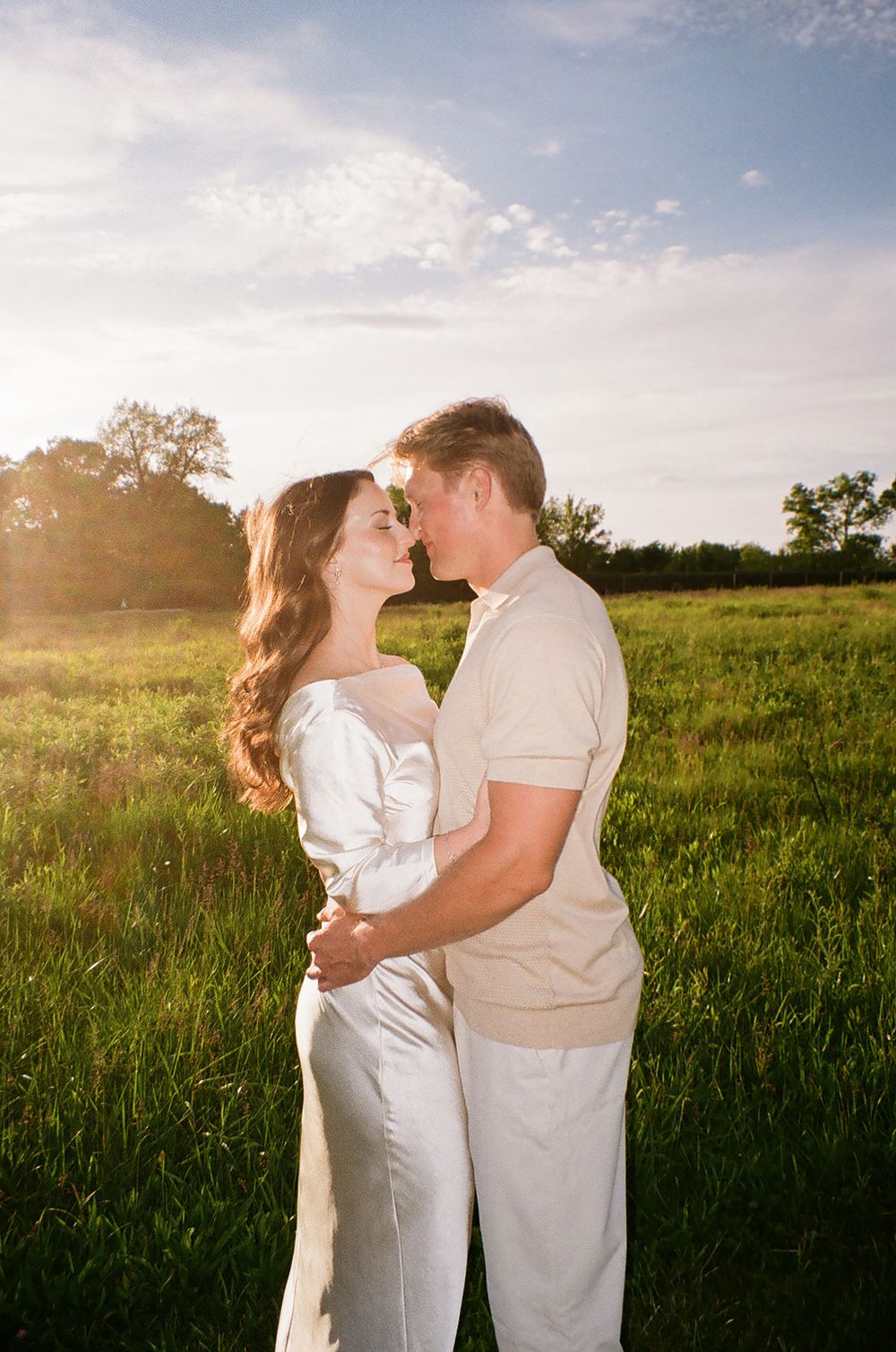 Romantic couple nearly kissing in golden sunset light in a lush green meadow on film.