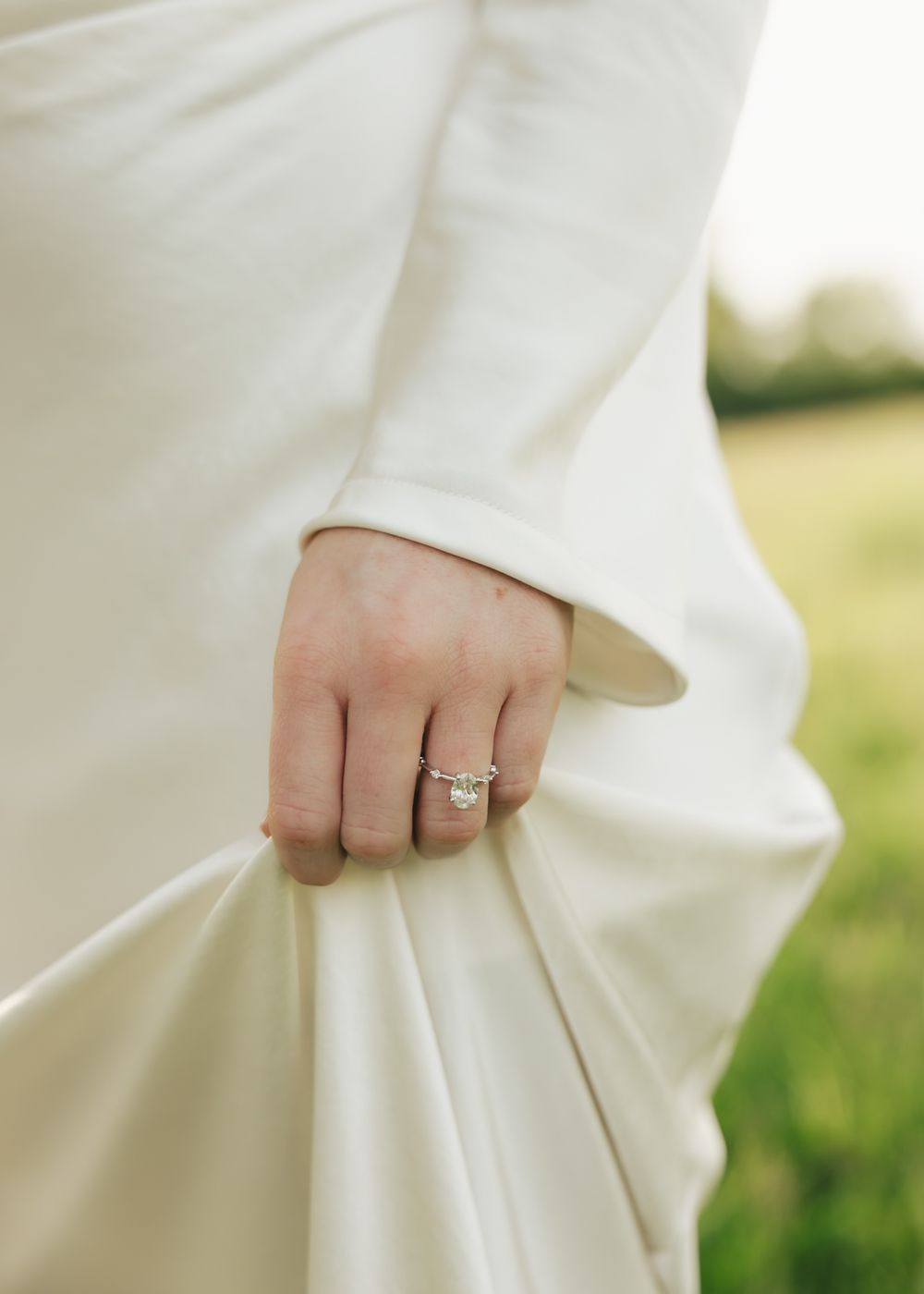 Close-up of an elegant emerald-cut diamond engagement ring on a womans hand holding a white dress.