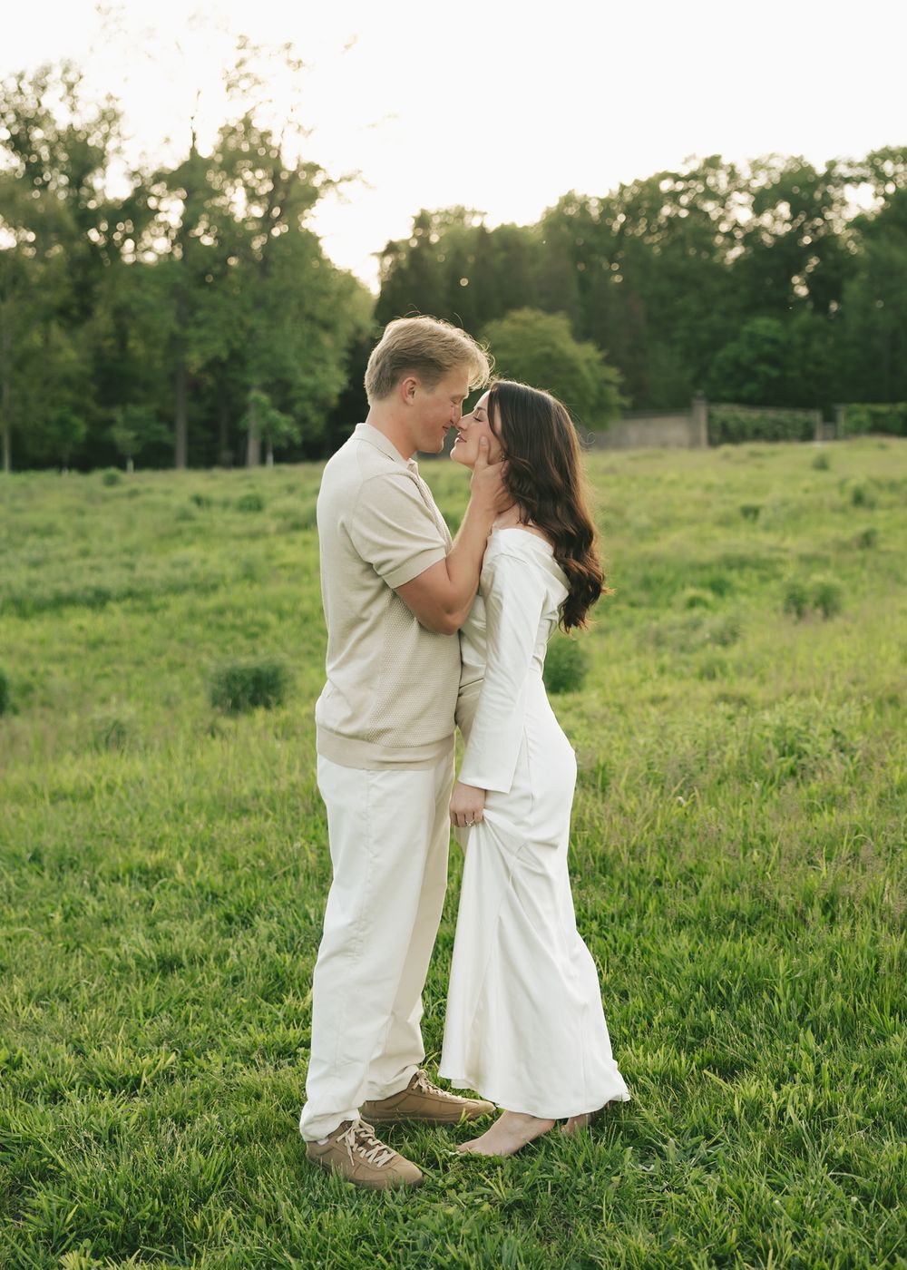 Couple embracing and sharing a tender moment in a lush green meadow during a golden hour engagement session.