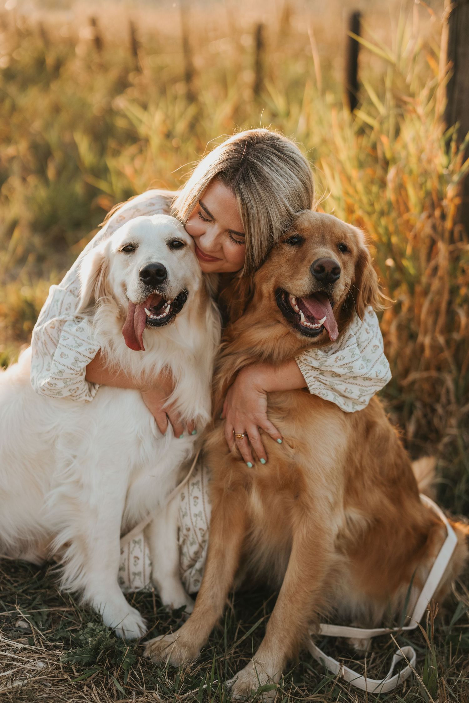 Two golden retriever dogs cuddle together with their owner in a sun-lit field during golden hour.