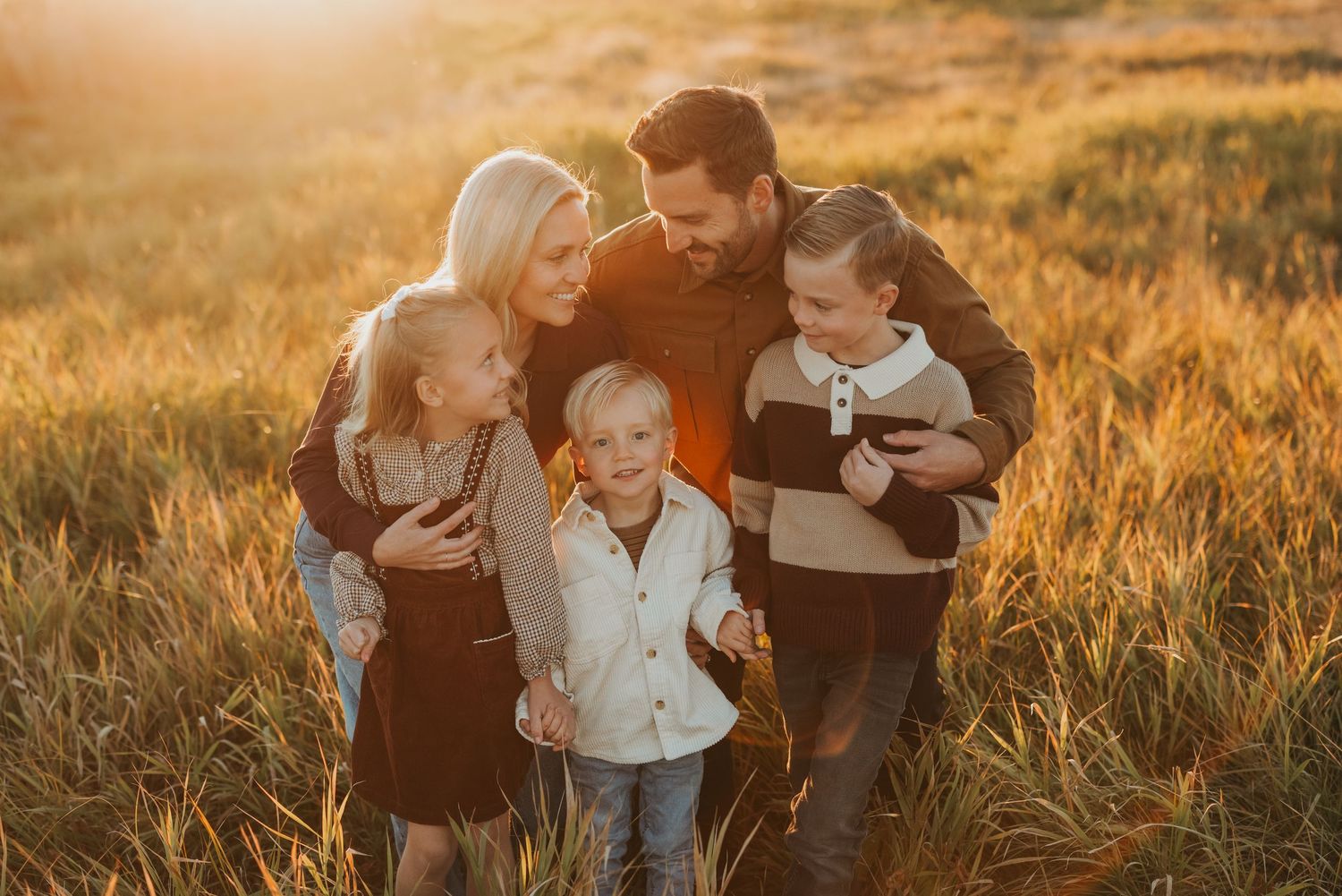 A family shares tender moments together in a golden wheat field at sunset.