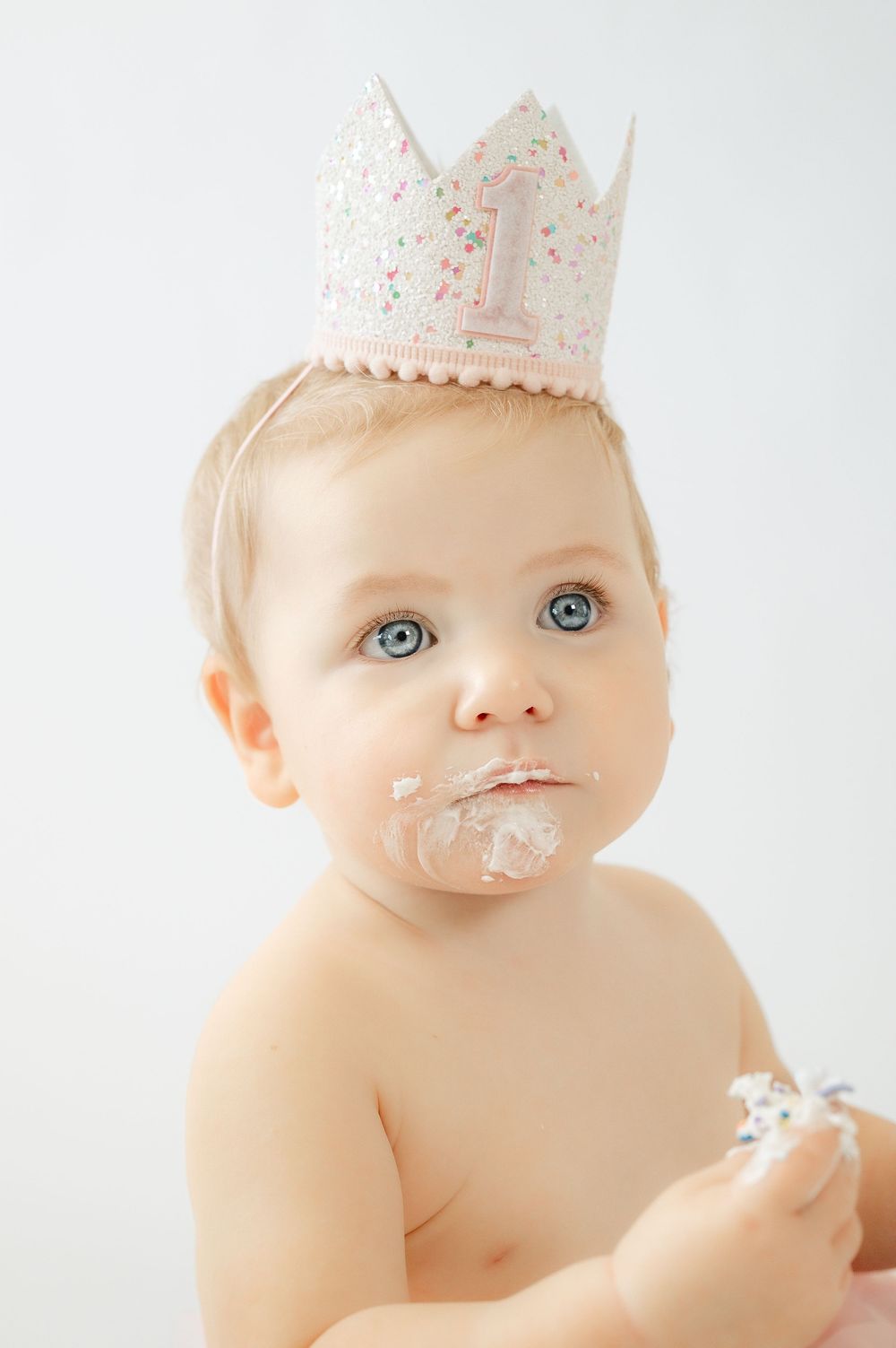Baby girl wearing a pink number 1 crown with cake on her face celebrating her first birthday.
