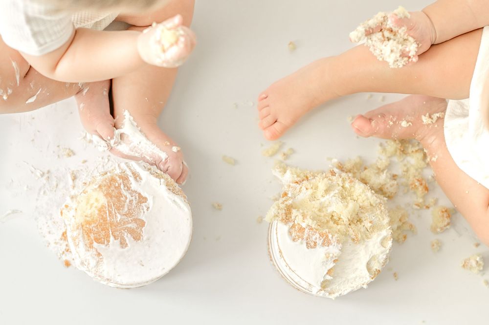 Two babies smashing white birthday cakes with their hands and feet during a cake smash photo session.
