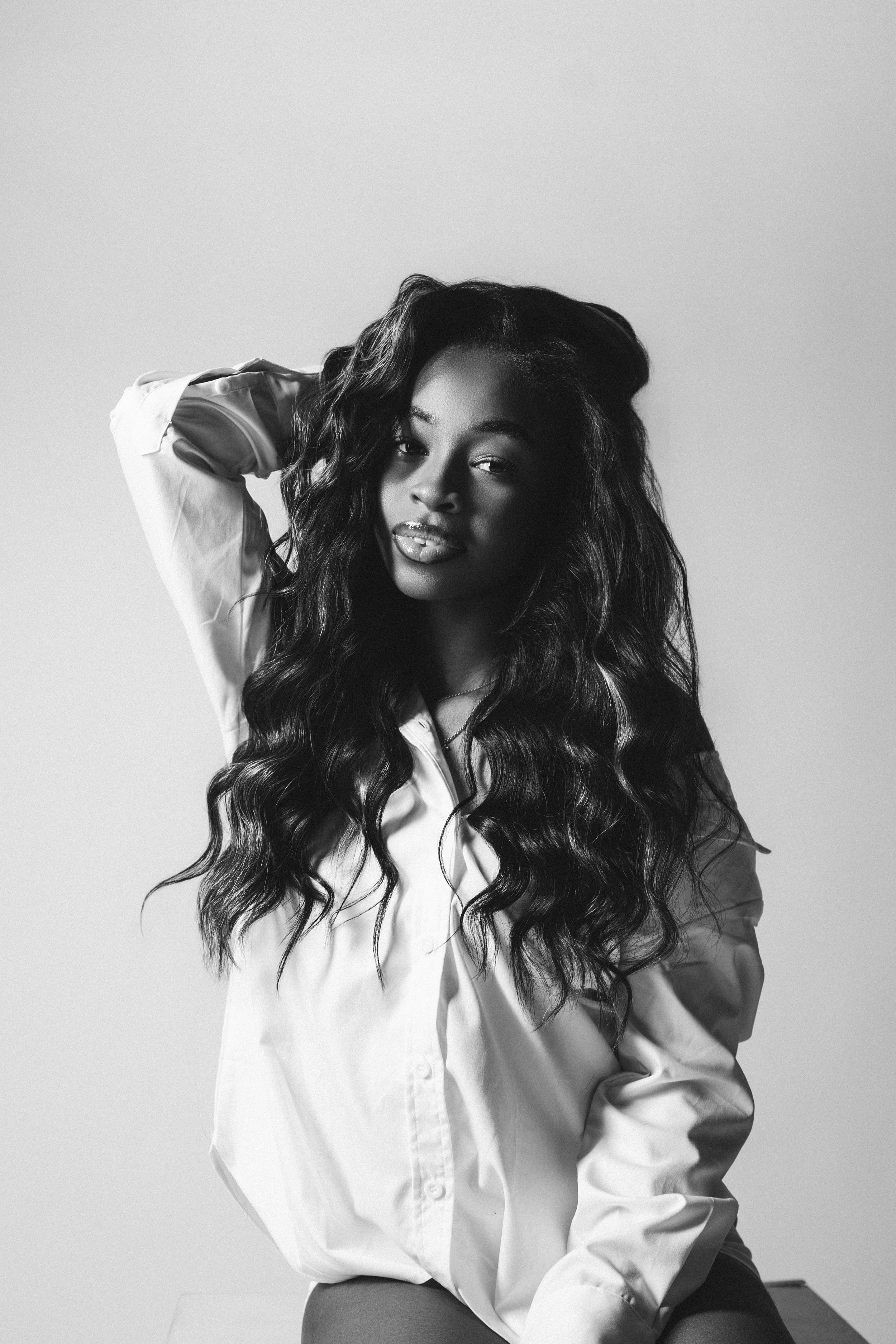 Black and white portrait of a woman with long wavy hair wearing a white button-down shirt against a plain background.
