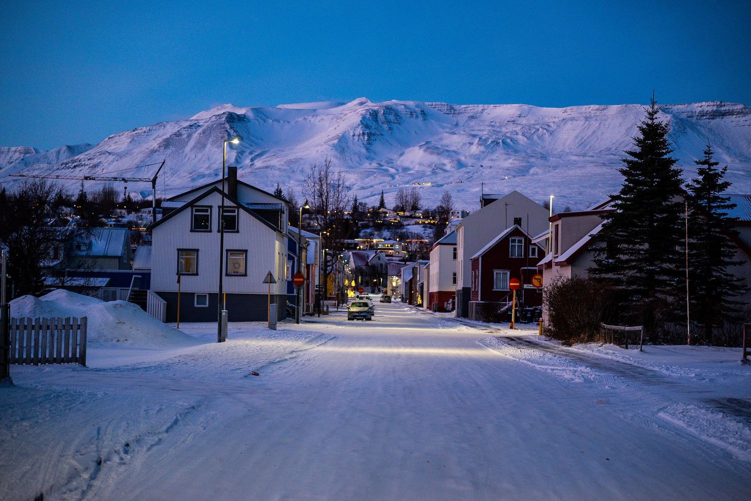 Snow covered mountain village illuminated at dusk with houses and buildings nestled against white slopes.