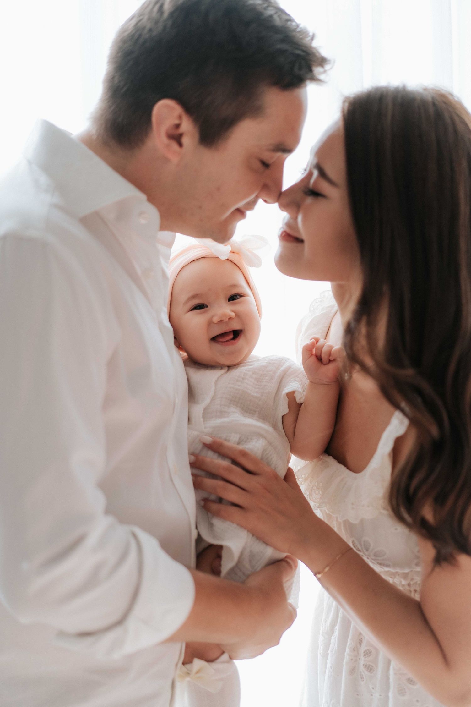 A sweet family photo series showing tender moments between parents and baby in white against a bright background.一組溫馨的家庭照片,展現了父母與寶寶在明亮背景下