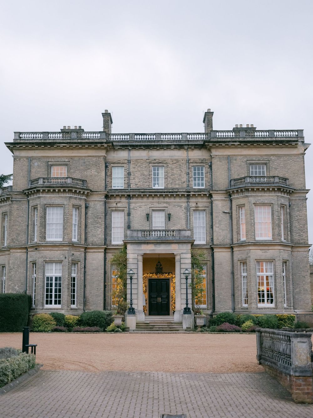 Panoramic exterior view of a grand historic manor house with symmetrical Georgian architecture and gravel driveway.