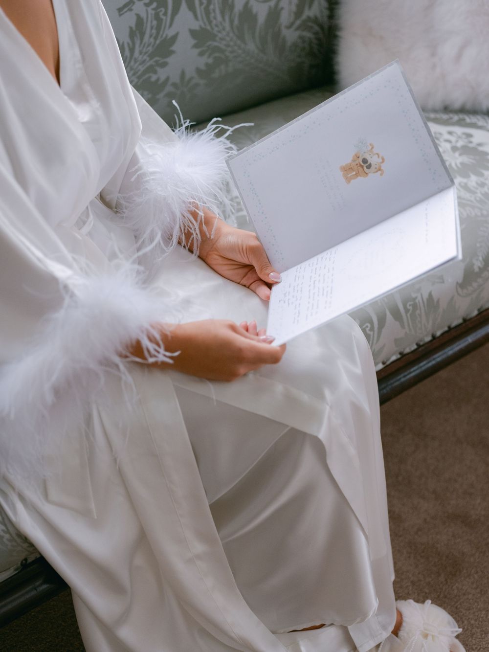 A person in a flowing white dress holds a letter or document while sitting on an elegant chair.