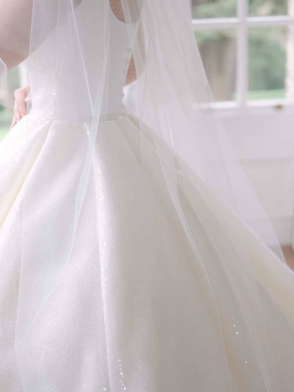 Close-up detail of a flowing white wedding dress with delicate veil and soft tulle fabric in natural window light.
