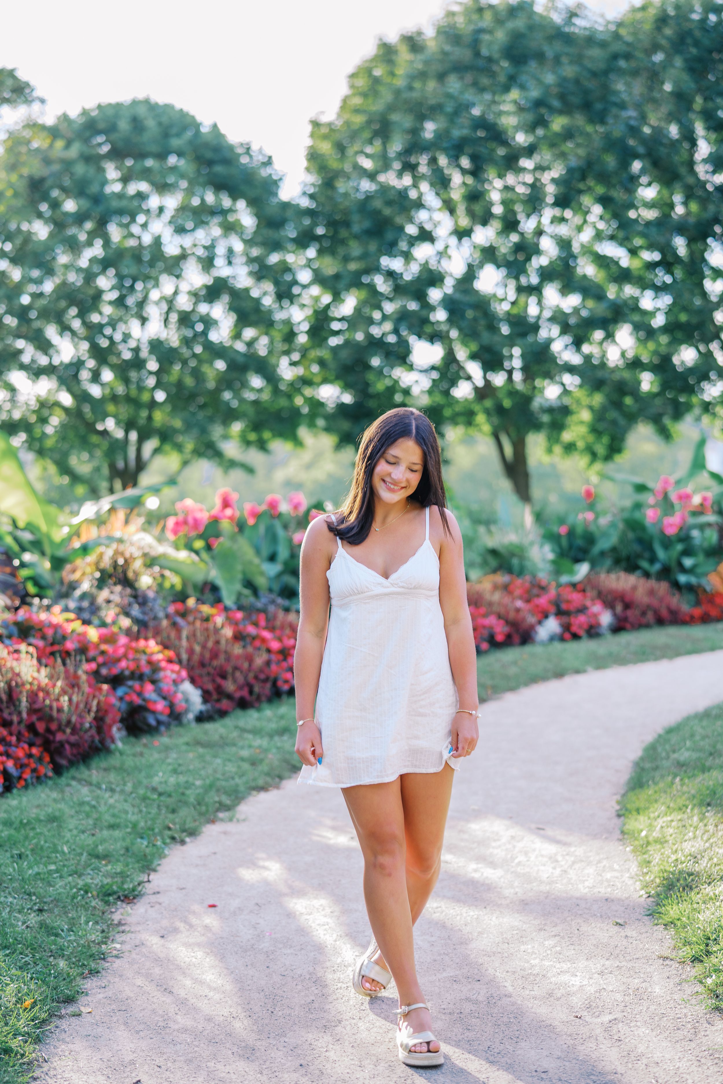Summer photoshoot along a winding garden path with vibrant red and pink flower beds.