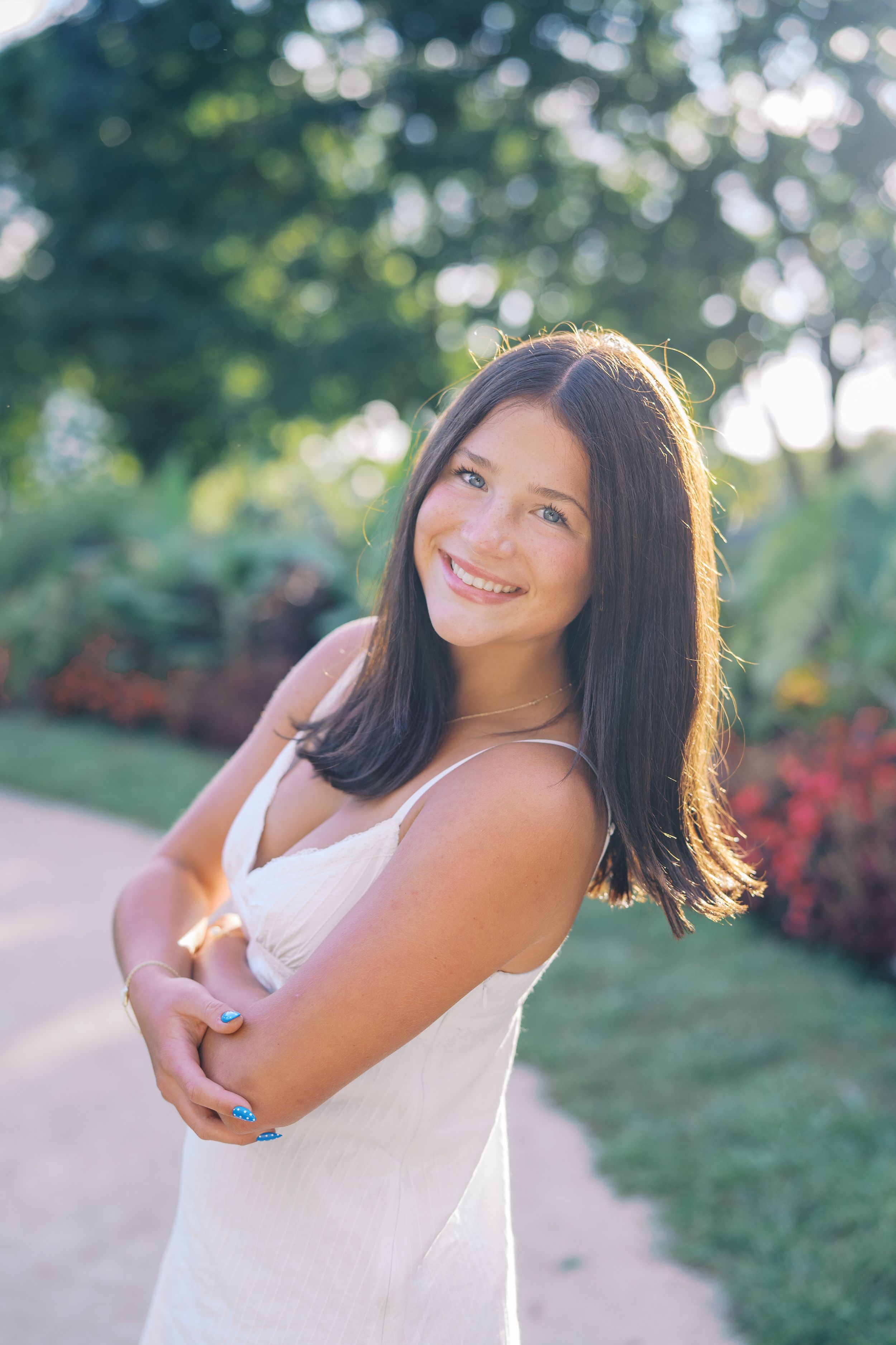Portrait of someone in white dress smiling warmly with sunlit garden in background.