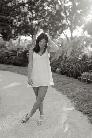 Black and white photo of person in white dress posing casually on garden path.