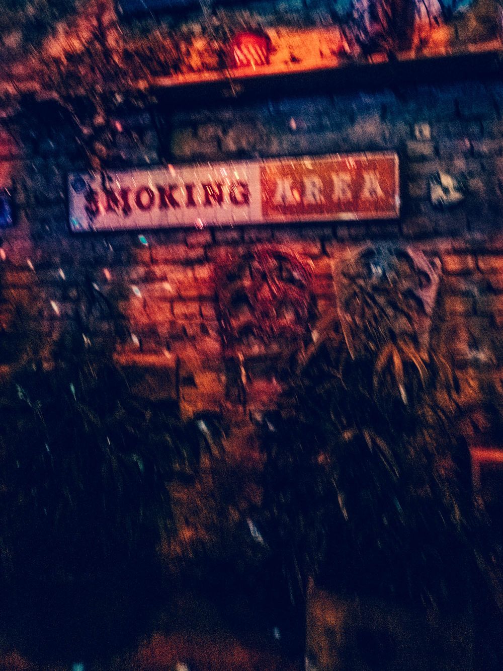 Dimly lit smoking area sign on a brick wall with moody red lighting and dark foliage.