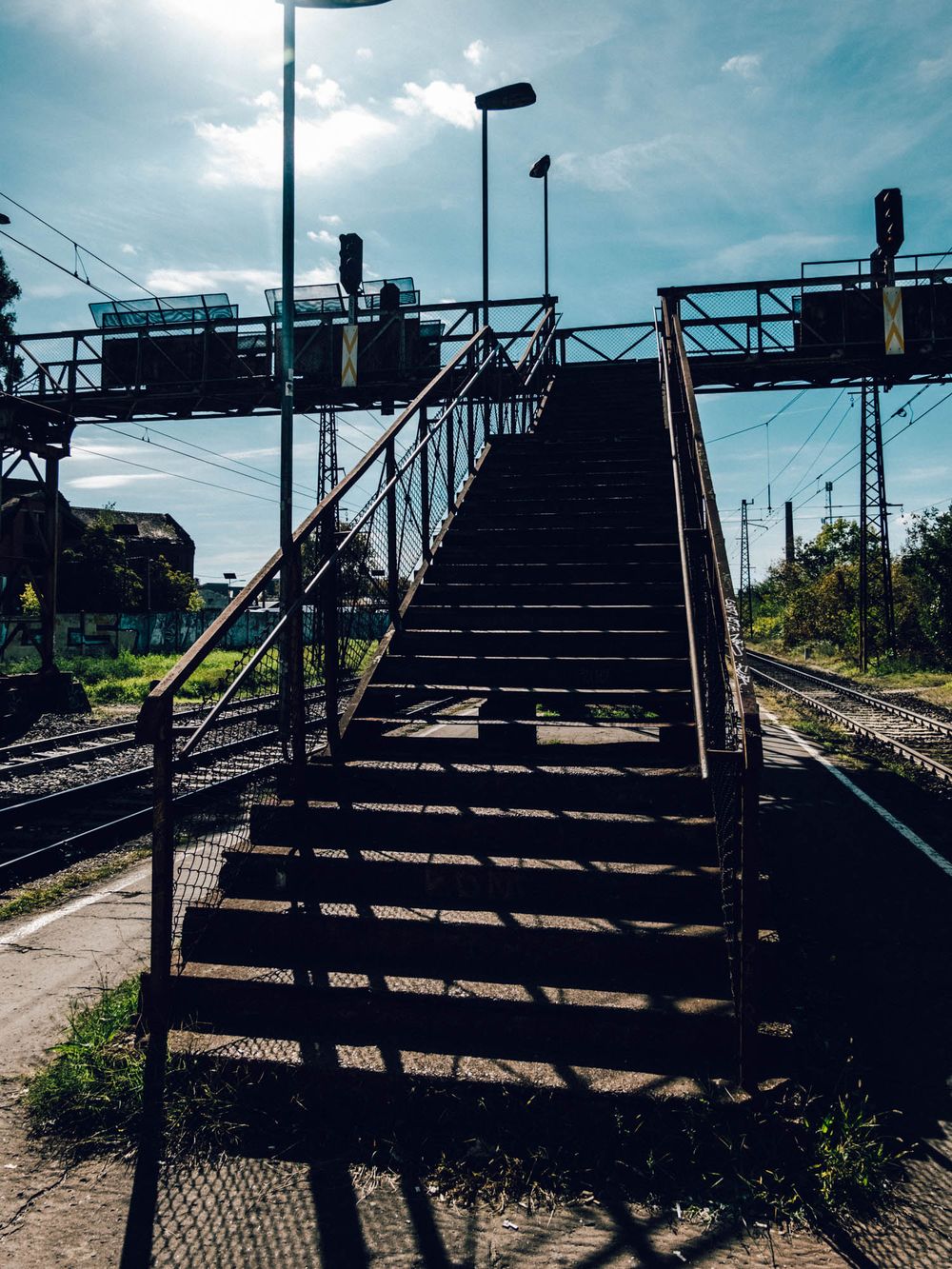 Metal staircase bridge over railway tracks under a partly cloudy sky at a train station.
