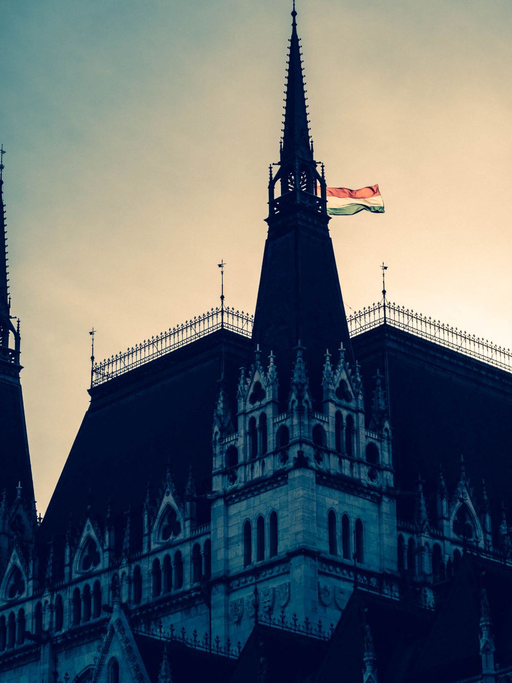 Hungarian Parliament Building gothic spire with national flag waving at sunset in Budapest, Hungary.