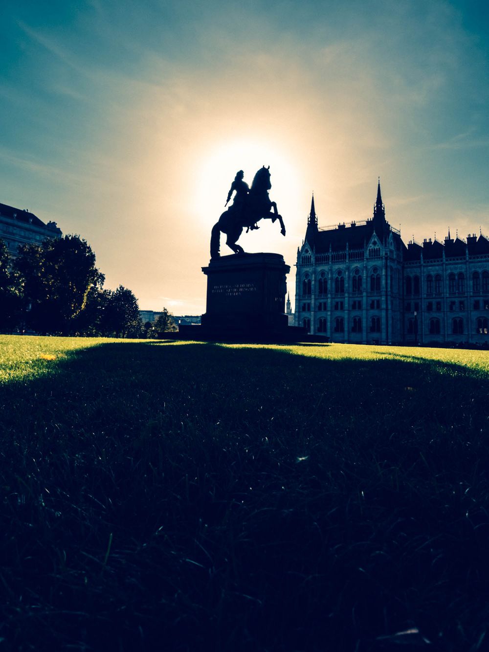 Silhouette of an equestrian statue backlit by the sun with the Hungarian Parliament Building in Budapest at dusk.
