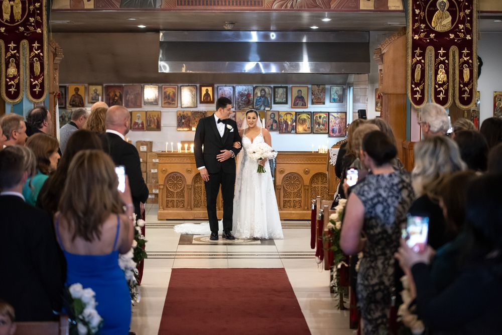 Bride and groom walk down the aisle of an Orthodox church decorated with religious icons.