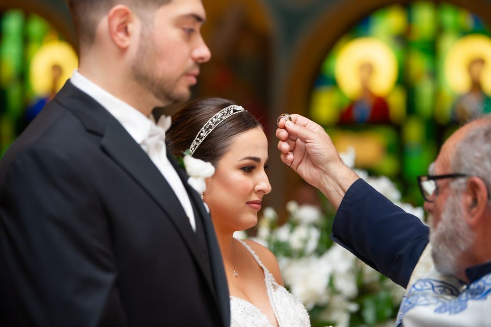 Orthodox priest places wedding crown on bride during traditional Greek Orthodox wedding ceremony.